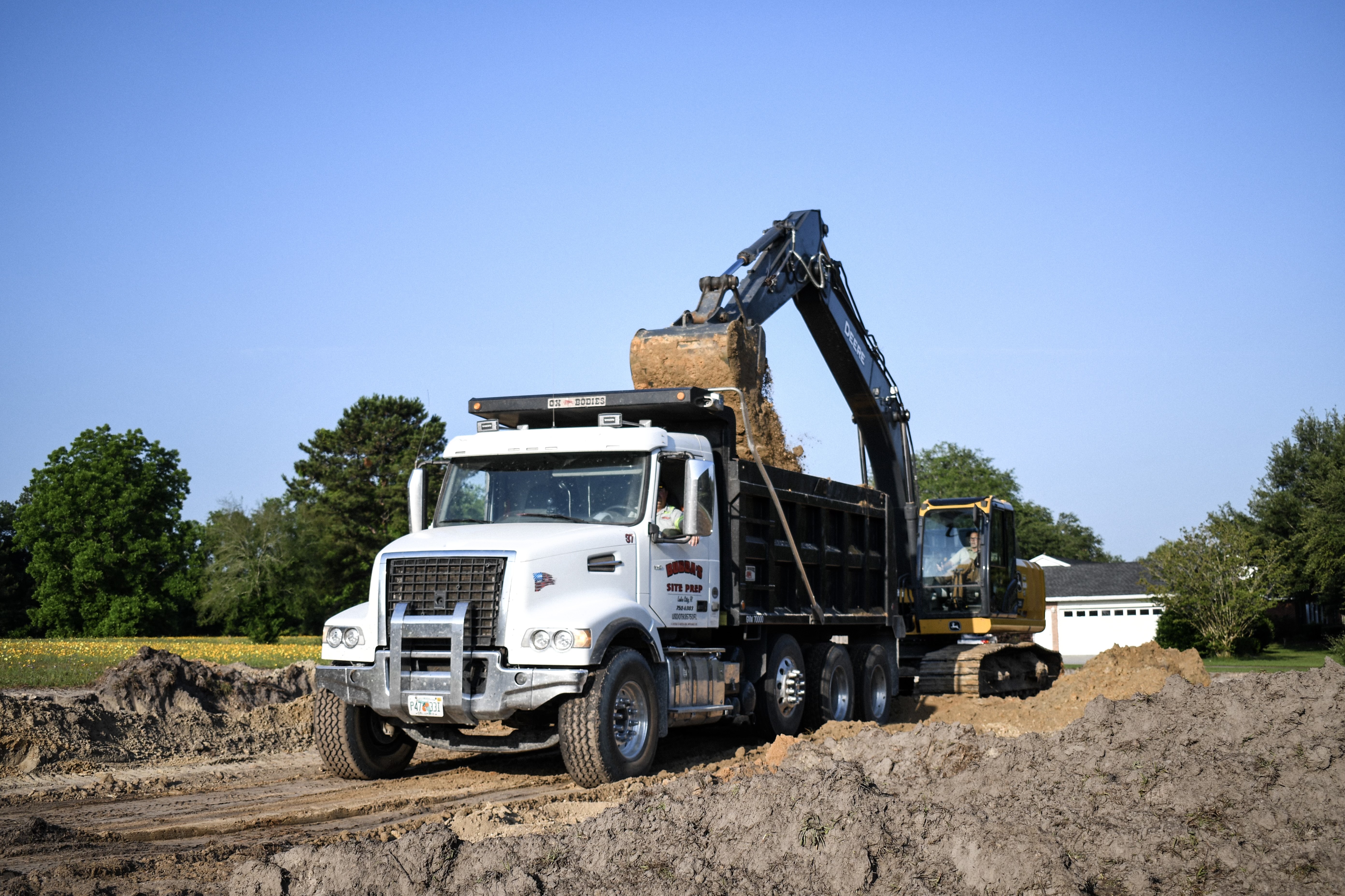 Excavator loading Bubba's branded dump truck — residential site work