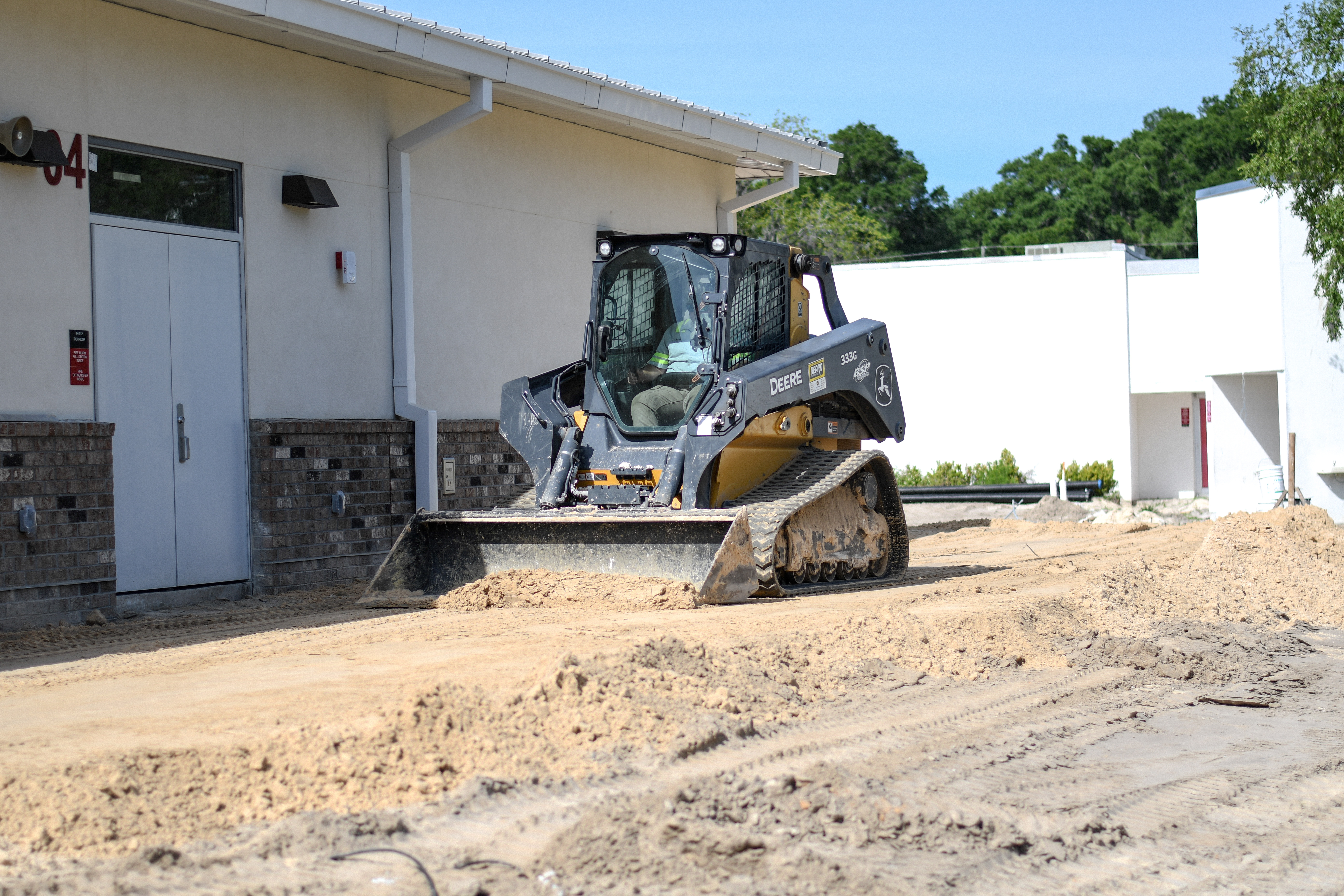 Skid steer performing finish grading at commercial building